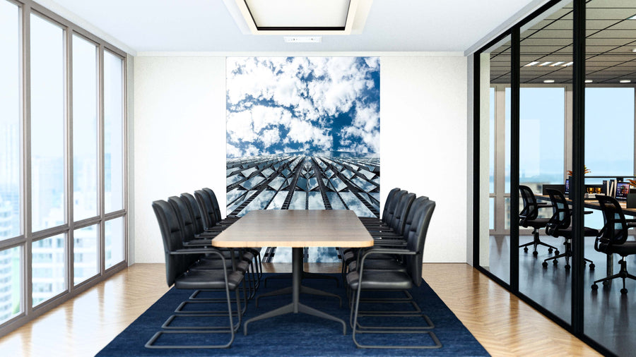 A modern conference room with a long wooden table, ten black chairs, glass walls, and a large Venting Wall Mural showing a skyscraper reflecting blue sky with clouds. The adjacent office is visible through glass; space features wooden floors and bright lighting.