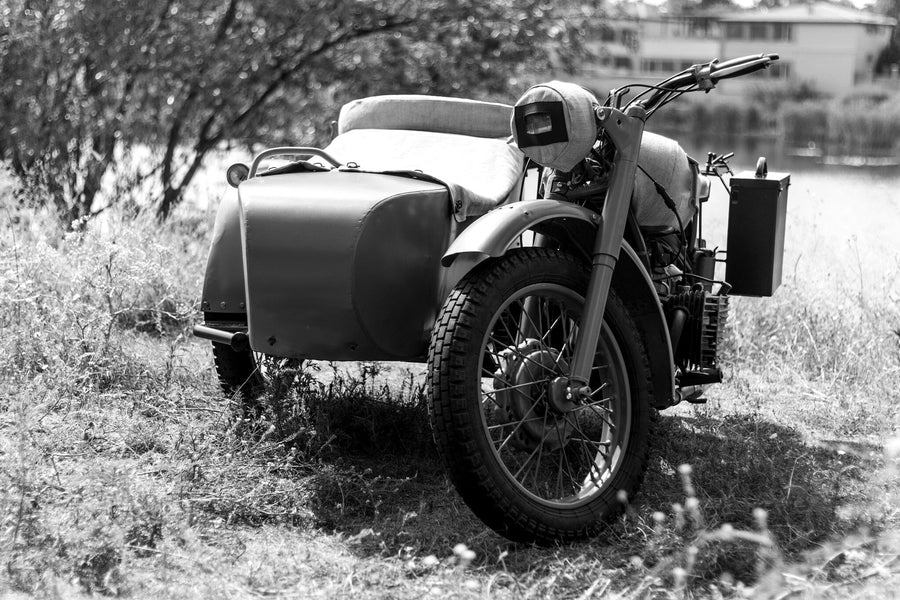 A modern garage with black cabinets, organized tools, and a vintage motorcycle. The back wall features the Vintage Sidecar Classic Wall Mural, showcasing an old motorcycle with a sidecar. Sunlight pours in from the open garage door.