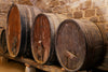 The Vintage Wooden Barrels Wall Mural depicts three large, weathered wooden barrels on a rack against a stone wall, exuding timeless charm. The metal bands suggest their role in storing wine or spirits, perfect for adding a vintage touch to any rustic cellar decor.