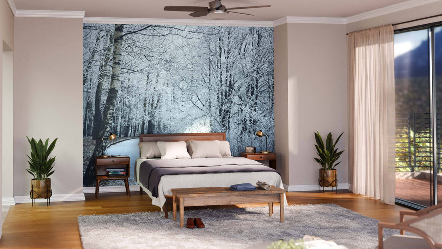 A modern bedroom features the Walkway in Winter Park Wall Mural behind a wooden bed with white and gray bedding. Nightstands, potted plants, a beige rug, and sheer-curtained windows complete this sunlit space.