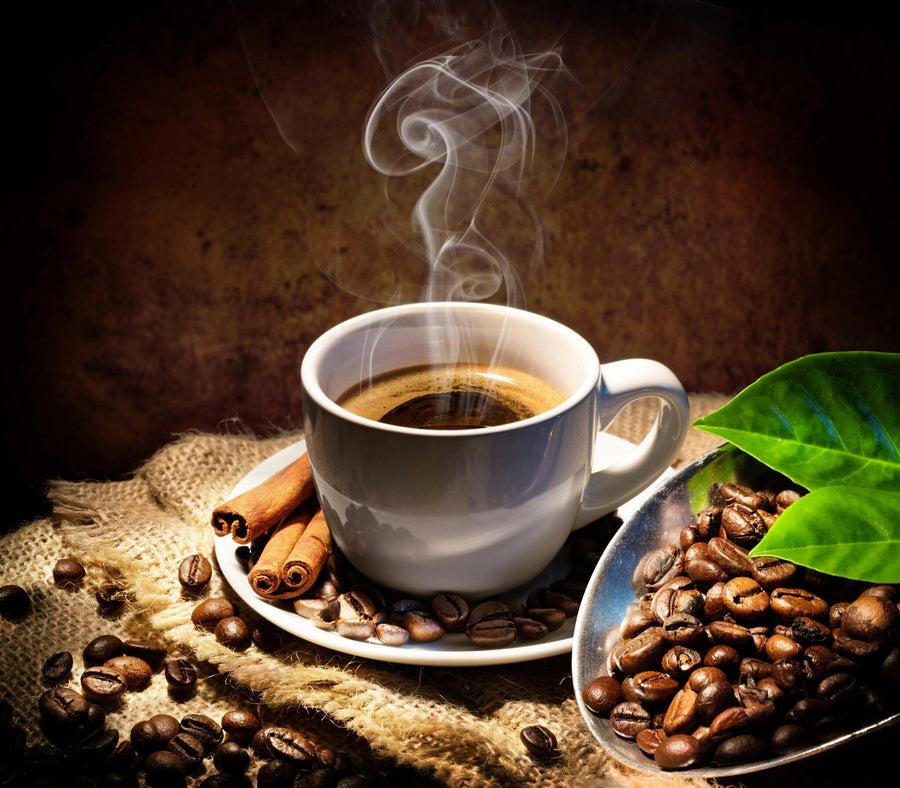 A modern, bright café with wooden tables and stools features a Warm Coffee Aesthetic Wall Mural depicting steaming coffee, beans, cinnamon sticks, and green leaves. Pendant lights hang above, plants accent tables, and large windows line one wall.