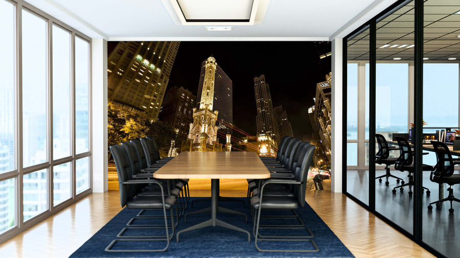 A modern conference room with a long wooden table and black chairs features the Water Tower Chicago Night Time Wall Mural. Glass walls divide the space, while wood flooring and natural light create a bright, professional atmosphere.