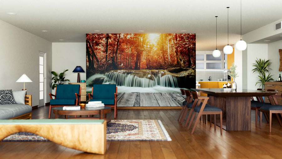 A modern living-dining room with wooden floors, teal chairs, and a large rug features the Waterfall in Autumn Forest Wall Mural on the back wall, bringing warmth and natural beauty to the space.