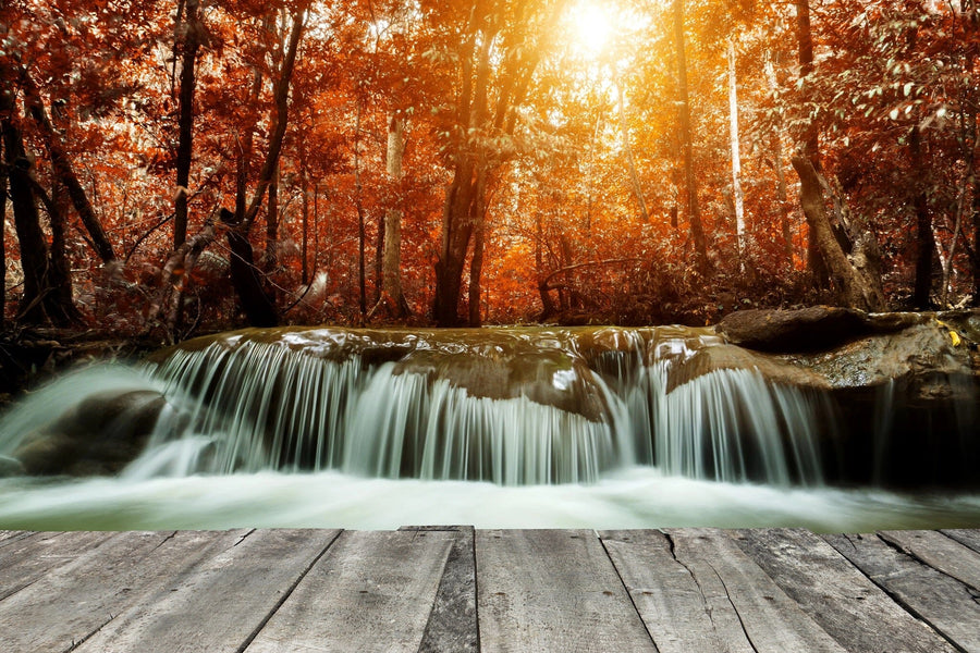 A modern living-dining room with wooden floors, teal chairs, and a large rug features the Waterfall in Autumn Forest Wall Mural on the back wall, bringing warmth and natural beauty to the space.