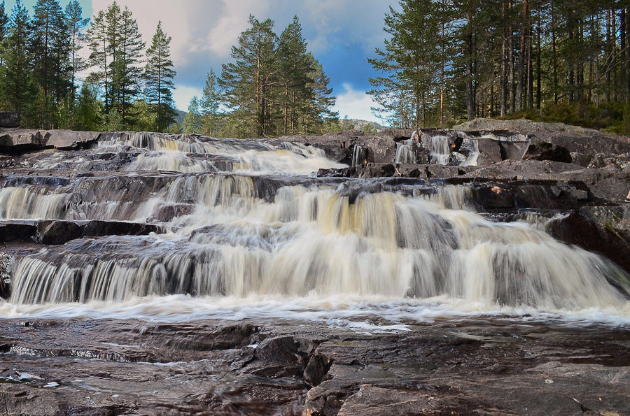 A modern open living and dining area with wooden floors, blue and wooden furniture, and pendant lights features the Waterfall in Forest Wall Mural, creating a natural, serene focal point with its imagery of cascading water and trees.