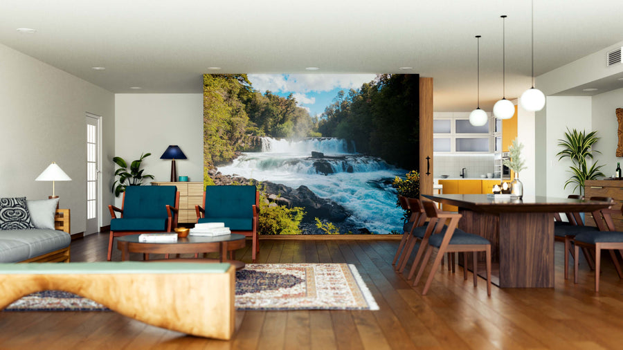 A modern open-plan living and dining room with wooden furniture, blue and green accents, features the "Waterfall of La Leona Wall Mural," a peel-and-stick decor piece that brings a natural, serene vibe to the contemporary space.