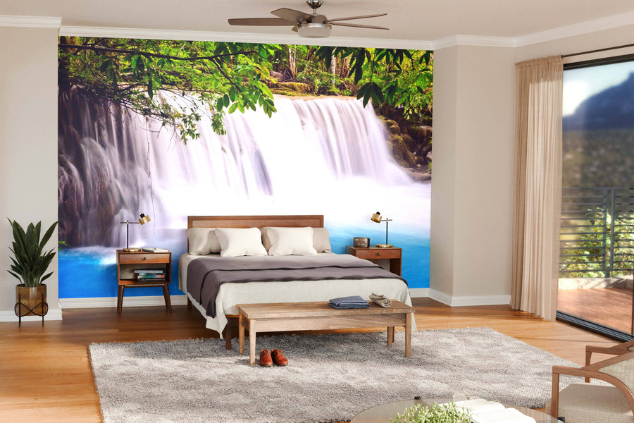 A modern living and dining room features wooden floors, teal chairs, a large dining table, and the Waterfalls Kanchanaburi Thailand Wall Mural. Pendant lights hang above the table, and natural light fills the inviting space.