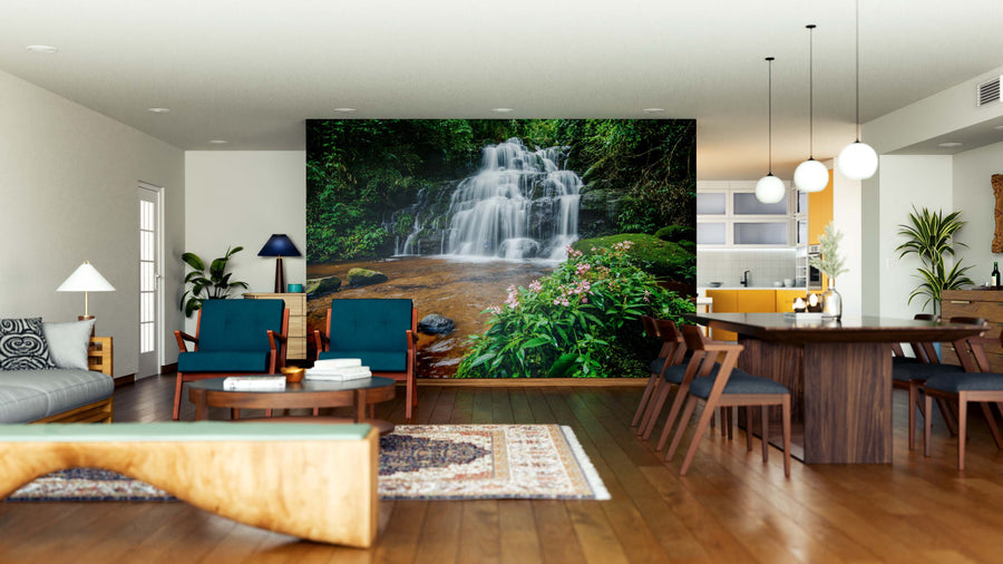 A modern living and dining room with wood floors, blue chairs, and a rug features the "Waterfalls in Thailand Wall Mural" on the main wall, bringing lush nature into the contemporary decor.