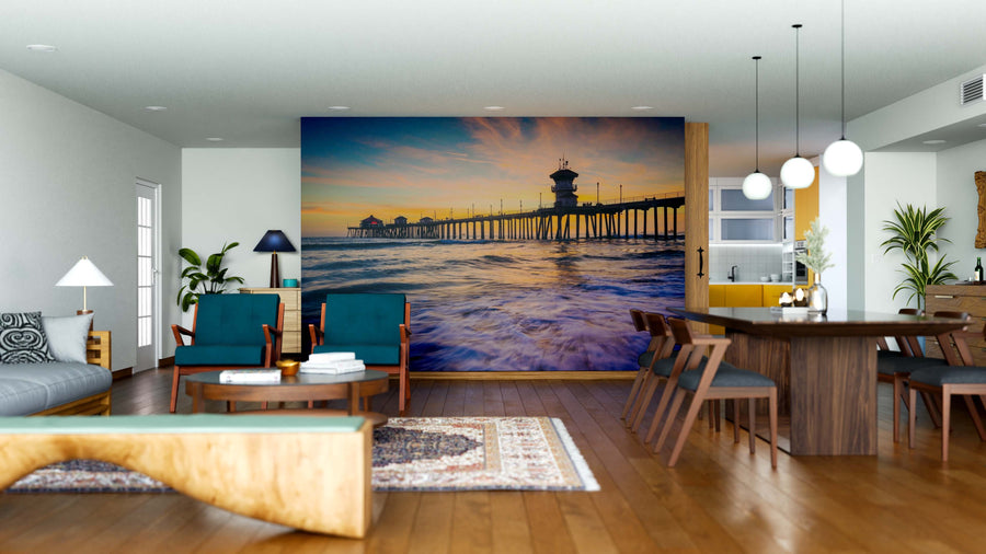 Modern living and dining room with wooden floors, teal chairs, and a large Waves in the Ocean Wall Mural depicting a sunset over the sea. Includes a wooden dining table, pendant lights, indoor plants, and cozy contemporary decor.