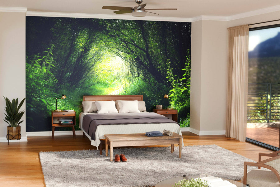 A modern bedroom showcases the Way in Deep Forest Wall Mural behind the bed. Wooden furniture, a plant, and a gray rug rest on hardwood floors, while glass doors fill the space with natural light.