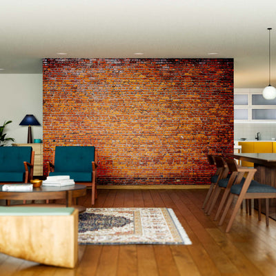 A modern open-concept living and dining area features wood floors, teal armchairs, a sofa, wooden coffee table, dining set, pendant lights, greenery, and a large accent wall with the Weathered Urban Texture Wall Mural—blending mid-century and contemporary decor.