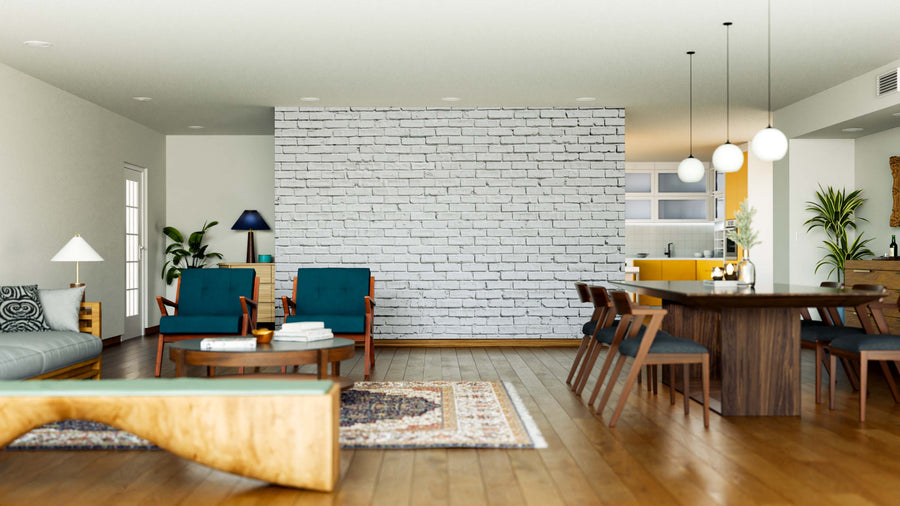 A modern open-plan living and dining area with wooden floors, teal armchairs, a gray sofa, rugs, a long wooden dining table with chairs, globe lights, indoor plants, a view of a yellow kitchen, and a White Brick Wall Mural accent.