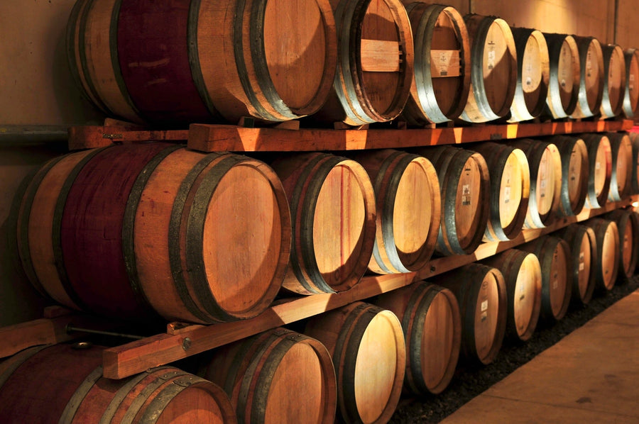 A cozy cafe features wooden tables, stools, small plants, and a warm atmosphere with sunlight from large windows. The highlight is the Wine Barrels Wall Mural depicting rows of wine barrels on the main wall.
