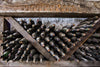 A rustic wine rack holds dusty wine bottles arranged in a crisscross wooden structure with necks facing outward. Above the rack, a decorative wooden panel complements Deposit photo's elegant "Wine Bottles Covered in Dust Wall Mural" adorning the stone wall.