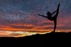 A woman performs a balancing yoga pose on one leg at sunset, her silhouette set against a vibrant backdrop of orange, pink, and purple. This dramatic view mirrors the serene energy captured in Deposit Photo's Woman Stretching Wall Mural.