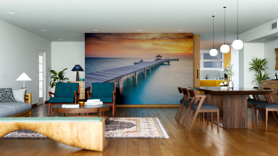 A modern living-dining area with wood floors, blue and wood furniture, pendant lights, and the Wood Bridge Wall Mural depicting a serene pier at sunset creates a tranquil, inviting atmosphere.