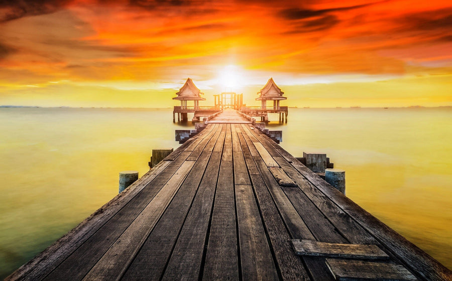 A bright, modern living-dining space with wood furniture and teal chairs features the Wooden Bridge Wall Mural, depicting a pier at sunset with warm orange tones for a dramatic focal point.