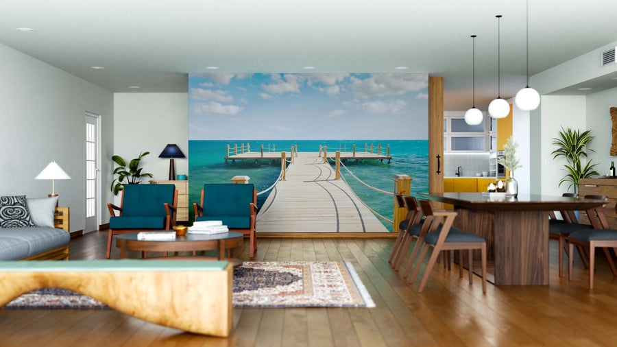 Spacious modern living and dining area with wood floors, teal chairs, and the Wooden Pier Wall Mural depicting a dock over turquoise ocean, creating an outdoor illusion. Eclectic decor, round lights, plants, and contemporary furniture accent the space.