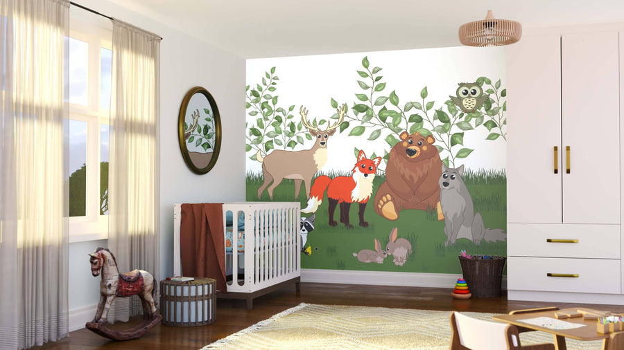 A cozy, modern nursery is brightened by the Woodland Animal Friends Wall Mural, displaying deer, fox, bear, owl, raccoon, rabbit, and wolf on green grass with leafy branches. A crib, rocking horse, basket, and toys furnish the sunlit space.