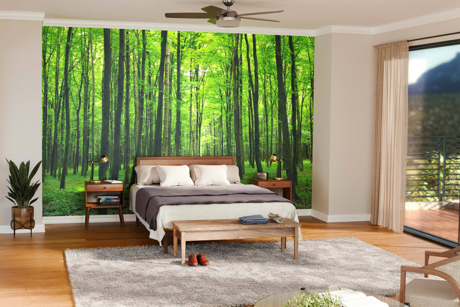 A modern open living-dining room features wood floors, green chairs, a dining table, and the Young Forest Wall Mural as a lush, nature-inspired focal point. Pendant lights hang above the table while natural light fills the space.