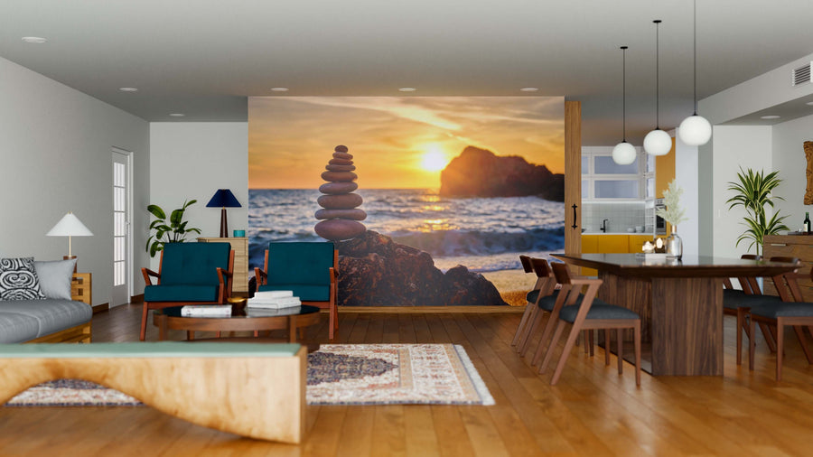 A modern open-plan living and dining area features wood furniture, teal chairs, pendant lights, and the Balance and Harmony Wall Mural showing a sunset over the ocean with stacked stones. Warm sunlight enhances this cozy, contemporary space.
