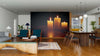 A modern open living and dining room with wooden floors, teal and wood furniture, a patterned rug, and a large Burning Candles Wall Mural creates a cozy, warm atmosphere. Pendant lights hang over the dining table by the bright kitchen.