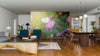 Modern open-plan living and dining area with wood flooring and mid-century furniture. The focal point is a large, vibrant Colorful Flowers Wall Mural. Pendant lights illuminate the dining table with the kitchen visible in the background.