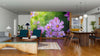 A modern open-plan living and dining area with wooden flooring, teal chairs, and a long table features the Cosmos Flowers in Garden Wall Mural—a vibrant, removable wallpaper showcasing close-up pink cosmos flowers as the room’s focal point.
