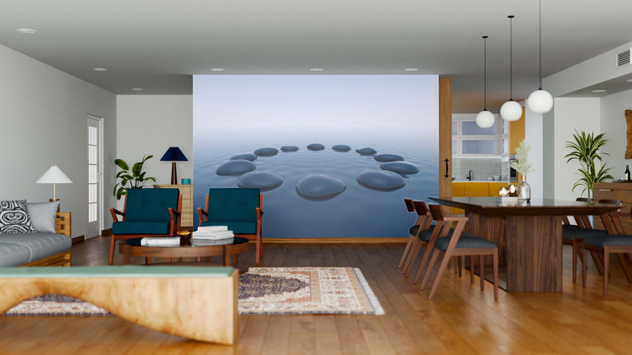 A modern open-concept living and dining area with wooden floors, teal chairs, a patterned rug, and the Pebbles in Water Wall Mural featuring black stones in a circle on calm water. Pendant lights hang above the wooden dining table and chairs.