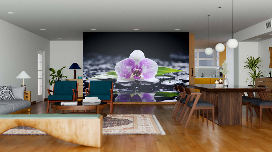 A modern living-dining room with wooden floors, blue chairs, and a large Still Flower Wall Mural featuring a pink orchid with water droplets. The stylish interior also includes a dark dining table, plants, pendant lights, and cozy carpet.