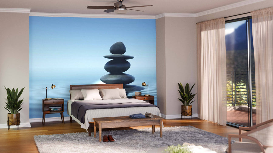 A modern bedroom showcases the Zen Stones Blue Sky Wall Mural behind the bed, accented by beige walls, wood floors, potted plants, and sheer-curtained sliding glass doors for a tranquil atmosphere.